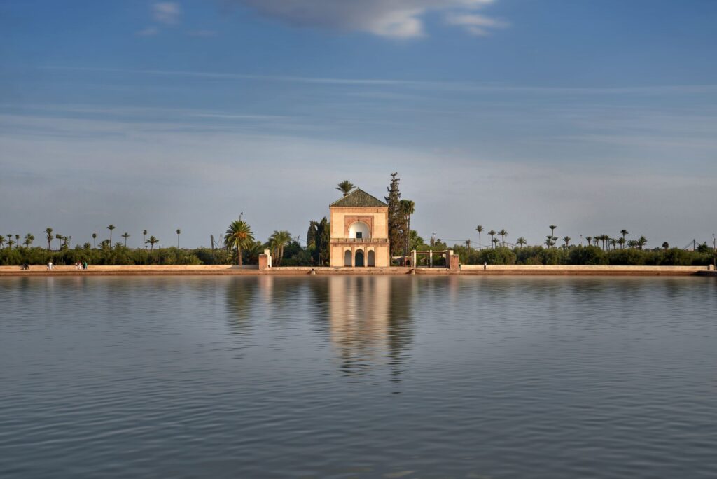 The historic green-roofed pavilion reflected in the large artificial lake of the Menara Gardens in Marrakech under a clear blue sky. Photo by Julia Volk on Pexels.